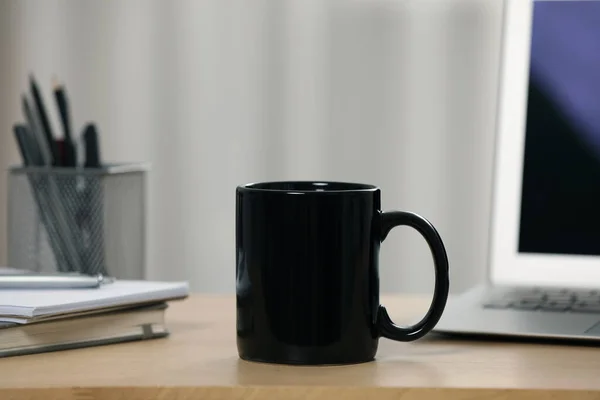 stock image Black ceramic mug, notebooks and laptop on wooden table at workplace