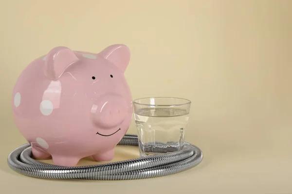 Water scarcity concept. Piggy bank, shower hose and glass of drink on beige background, space for text