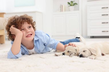 Evdeki beyaz halıda sevimli köpek yavrularıyla uzanan küçük çocuk.