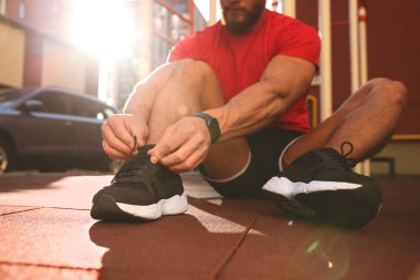 Güneşli bir günde spor salonunda antrenmandan önce ayakkabı bağı bağlayan adam, yakın çekim.