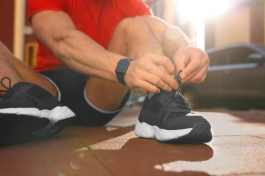 Güneşli bir günde spor salonunda antrenmandan önce ayakkabı bağı bağlayan adam, yakın çekim.