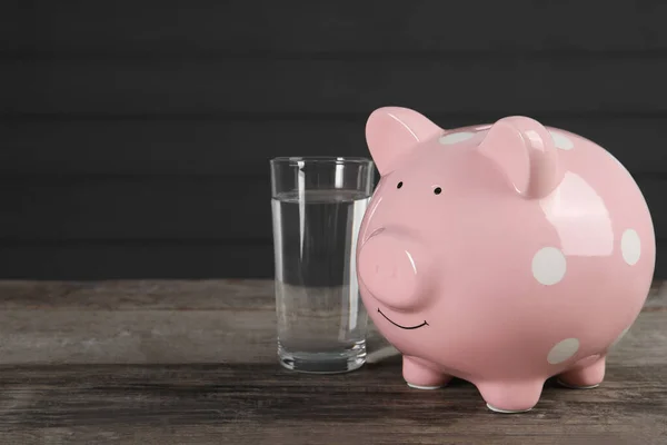 Water scarcity concept. Piggy bank and glass of drink on wooden table, space for text