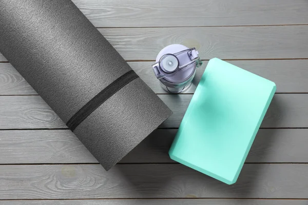 Exercise mat, yoga block and bottle of water on grey wooden floor, flat lay