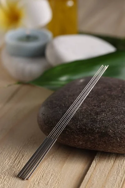 Acupuncture needles and spa stone on wooden table
