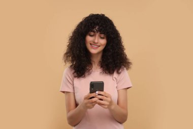 Bej arka planda akıllı telefon kullanan mutlu genç kadın.