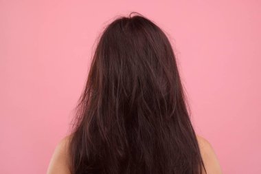 Pembe arka planda saçları zarar görmüş bir kadın.
