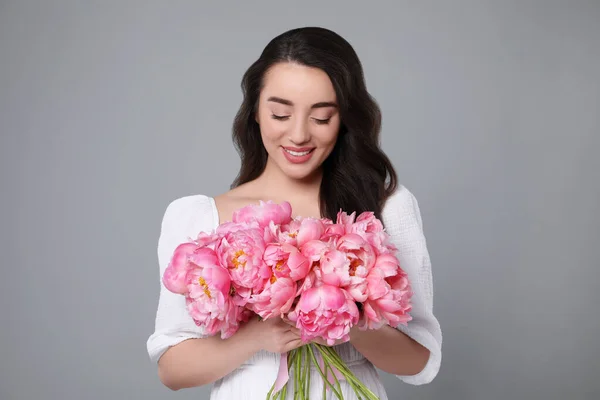 灰色の背景にピンクのコニーの花束が付いている美しい若い女性 — ストック写真