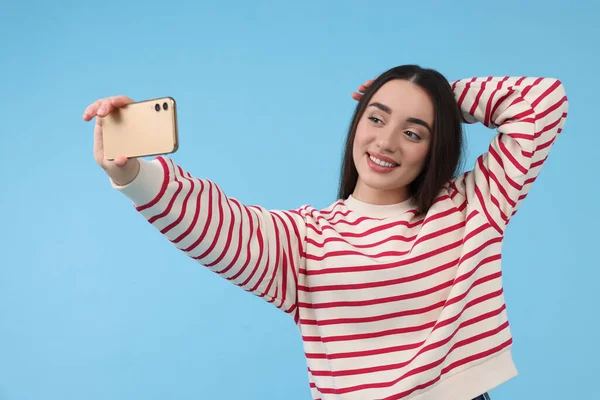 Uśmiechnięta Młoda Kobieta Robi Selfie Smartfonem Jasnoniebieskim Tle — Zdjęcie stockowe