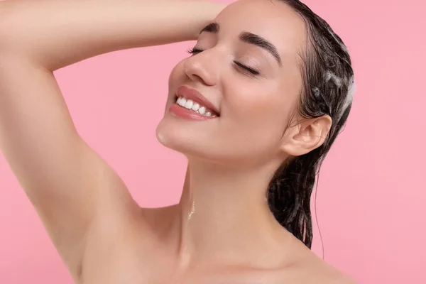 Portrait of beautiful happy woman washing hair on pink background
