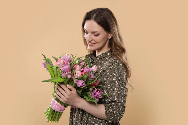ベージュの背景に美しいチューリップの花束を保持する幸せな若い女性 — ストック写真