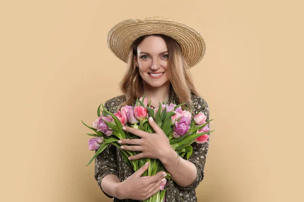 幸せな若いです女性でわら帽子保持花束の美しいですチューリップオンベージュ背景 — ストック写真