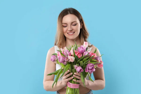 ライトブルーの背景に美しいチューリップの花束を持つ幸せな若い女性 — ストック写真