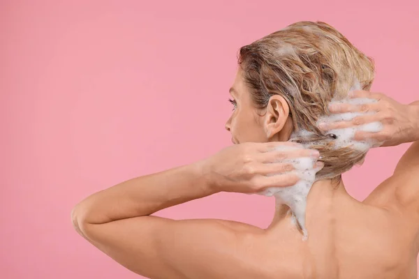 Woman washing hair on pink background, back view. Space for text