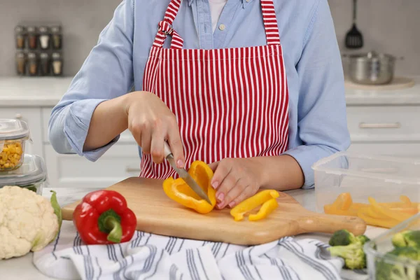 Woman cutting bell pepper near food storage containers at table in kitchen, closeup