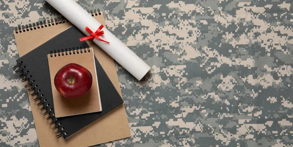Military education. Notebooks, apple and diploma on camouflage background, flat lay with space for text