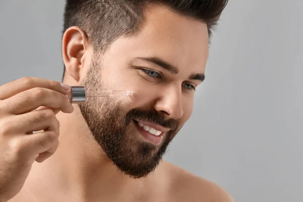 Schöner Mann Der Kosmetisches Serum Auf Das Gesicht Auf Grauem — Stockfoto