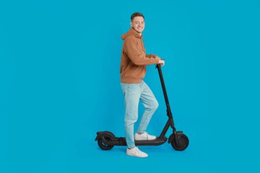 Açık mavi arka planda modern elektrikli scooter kullanan mutlu adam.