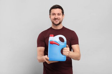 Açık gri zemin üzerinde mavi sıvı bulunan teneke kutu tutan adam.