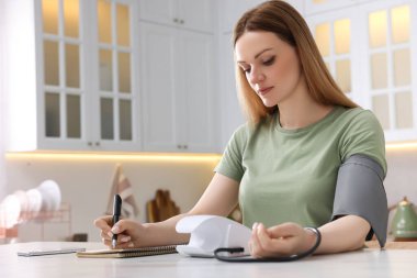 Kadın kan basıncını ölçüyor ve not defterine yazıyor. Mutfakta, mesaj için yer var.