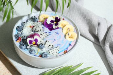 Taze meyve, yabanmersini ve çiçeklerle süslü nefis bir meyve suyu kasesi. Renkli masa, yakın plan.