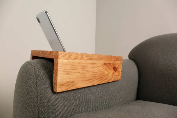 Smartphone on sofa with wooden armrest table in room. Interior element