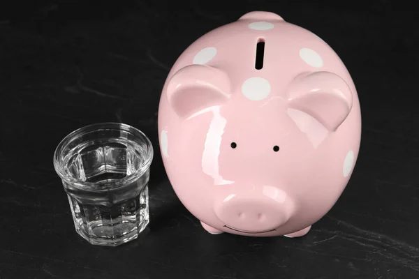 Water scarcity concept. Piggy bank and glass of drink on dark table