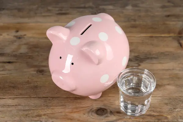 Water scarcity concept. Piggy bank and glass of drink on wooden table