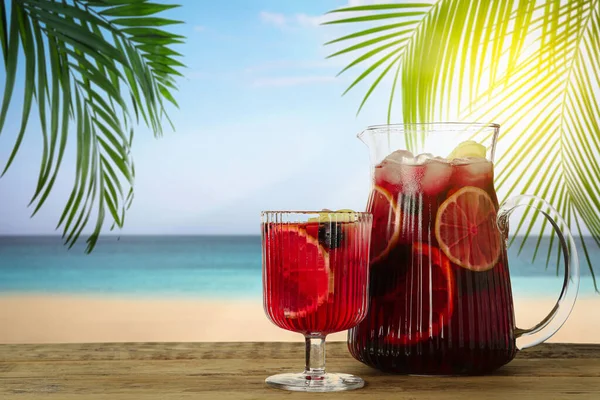 Refreshing Red Sangria on wooden table near sea, space for text