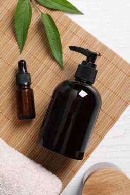 Bir şişe kozmetik ürünü ve yapraklar beyaz ahşap masada, düz yerde.