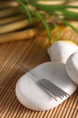 Bambu hasırı üzerinde akupunktur iğneleri ve spa taşları