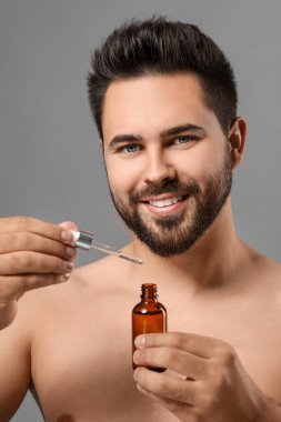 Gri arka planda kozmetik serumu olan yakışıklı bir adam.