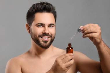 Gri arka planda kozmetik serumu olan yakışıklı bir adam.