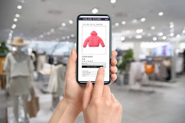 Kadın dükkânı ziyaret ediyor. Kapalı mekanda ceket siparişi veriyor. Web sitesi aygıt ekranında çevrimiçi kaydet