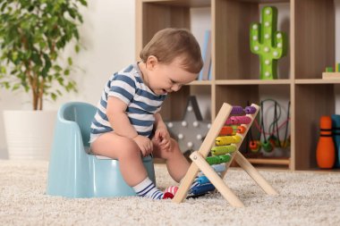 İçeride plastik bebek lazımlığında oturan abaküslü küçük çocuk.