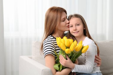 Anne ve şirin kızı evdeki kanepede sarı lalelerle oturuyorlar. Metin için boşluk