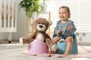 Küçük çocuk ve oyuncak ayı içeride plastik bebek tuvaletlerinde oturuyorlar.
