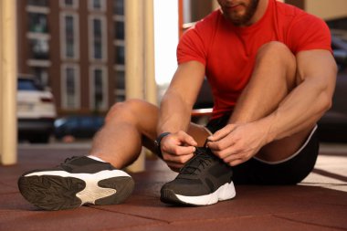 Güneşli bir günde spor salonunda antrenmandan önce ayakkabı bağı bağlayan adam, yakın çekim.