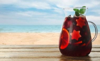 Deniz kenarındaki ahşap masada Red Sangria tazeleniyor, metin için yer var.
