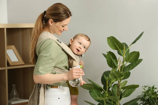 Matka Spryskiwanie Roślin Domowych Wodą Podczas Trzymania Dziecka Temblaku Nosidełko — Zdjęcie stockowe