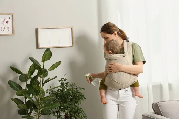 Mutter Besprüht Zimmerpflanzen Mit Wasser Während Sie Ihr Kind Tragetuch — Stockfoto
