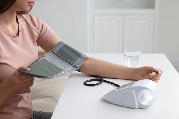 Woman measuring blood pressure with tonometer indoors, closeup