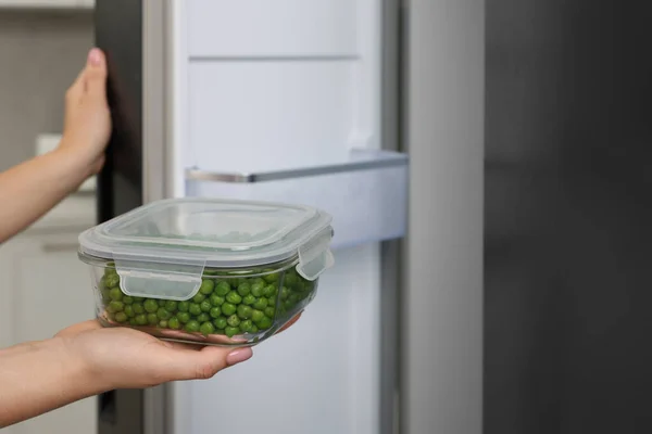 Woman putting container with tasty peas into fridge, closeup and space for text. Food storage