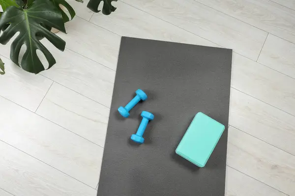 Exercise mat, yoga block and dumbbells on floor indoors, top view