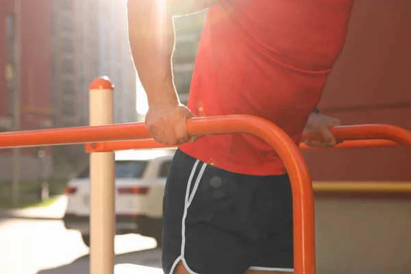 Man training on parallel bars at outdoor gym on sunny day, closeup