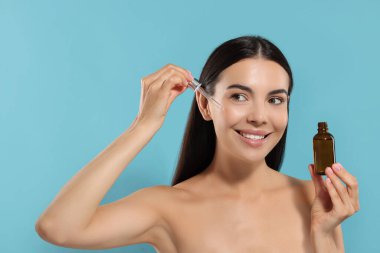 Güzel genç bir kadın açık mavi arka planda yüzüne serum sürüyor.