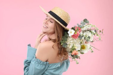Hasır şapkalı güzel bir kadın pembe arka planda bir buket çiçekle