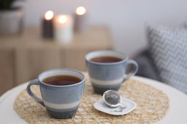 Cups of tea and snap infuser with dry leaves on white coffee table indoors, space for text clipart