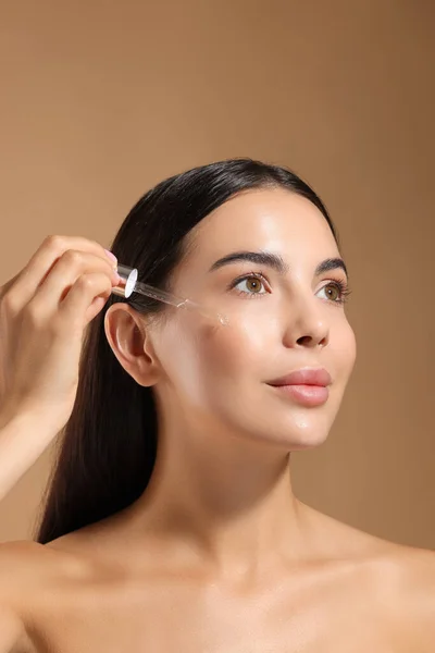 Beautiful Young Woman Applying Serum Her Face Beige Background — Stock Photo, Image