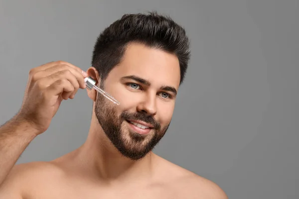 Schöner Mann Der Kosmetikserum Auf Gesicht Auf Grauem Hintergrund Aufträgt — Stockfoto