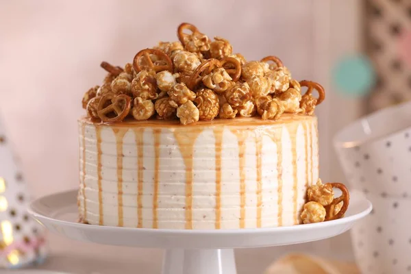 Caramel drip cake decorated with popcorn and pretzels against blurred background, closeup